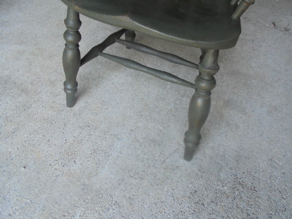 A low-backed wooden captains chair painted in dark green, featuring turned spindles, a curved armrest, and a shaped seat. View V