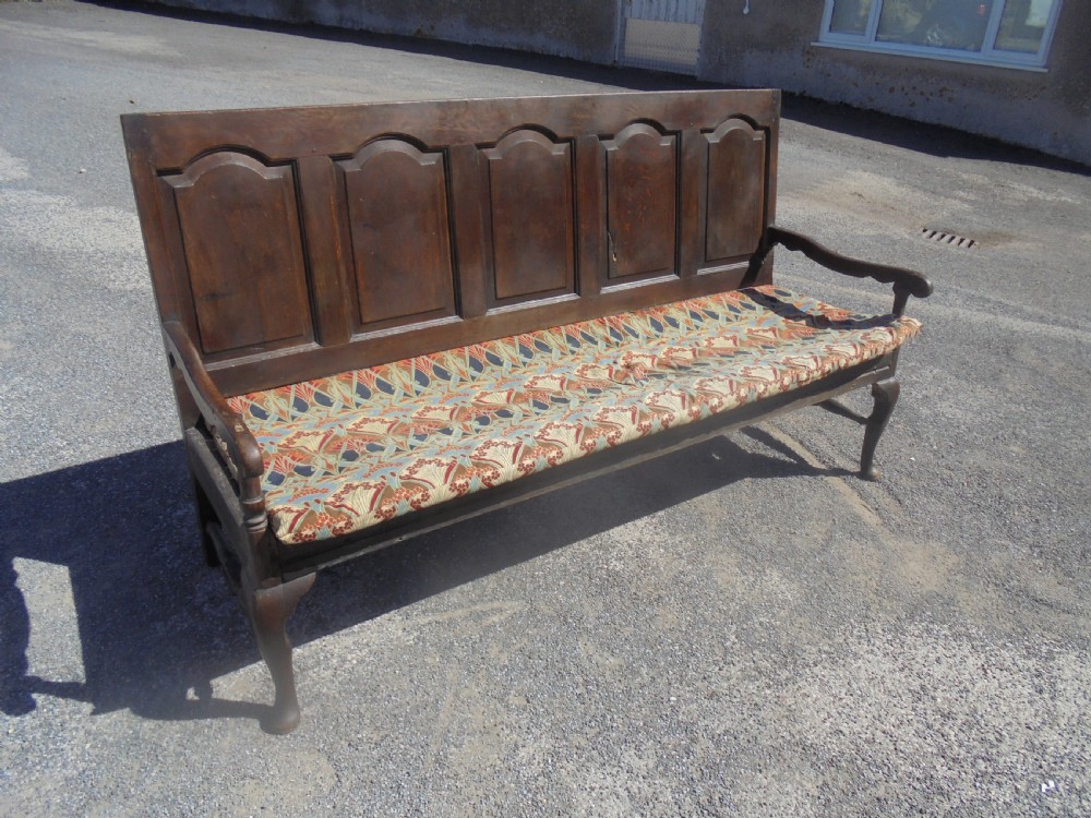 A dark oak wooden settle featuring five raised arched back panels, open curved armrests, cabriole front legs, and a patterned fabric seat cushion. View II