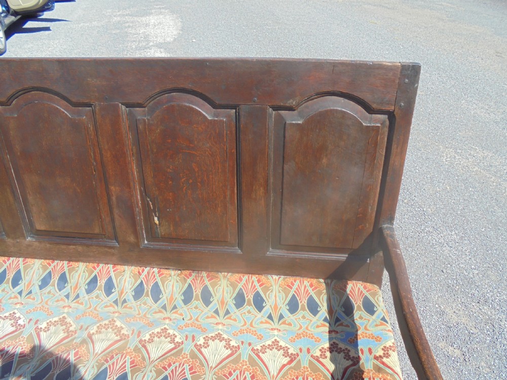 A dark oak wooden settle featuring five raised arched back panels, open curved armrests, cabriole front legs, and a patterned fabric seat cushion. View IV