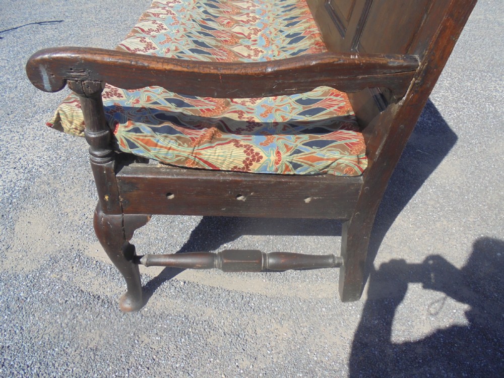 A dark oak wooden settle featuring five raised arched back panels, open curved armrests, cabriole front legs, and a patterned fabric seat cushion. View VII