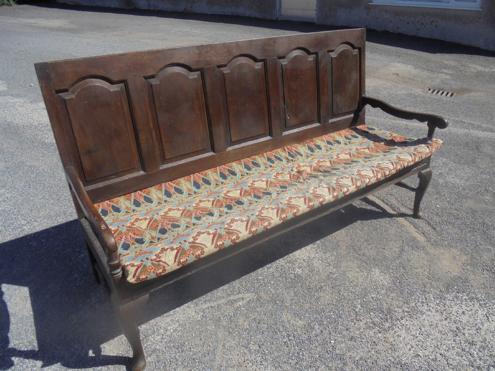 A dark oak wooden settle featuring five raised arched back panels, open curved armrests, cabriole front legs, and a patterned fabric seat cushion. View VIII