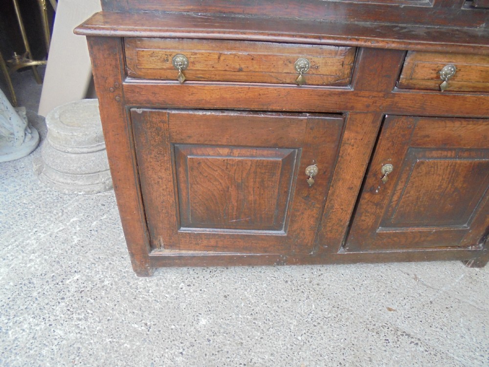 An early dark oak two-tier press cupboard featuring double geometric panelled doors, two drawers with brass teardrop handles, and turned drop finials. View III