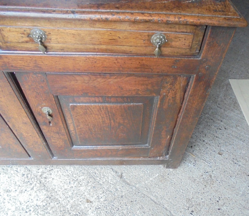 An early dark oak two-tier press cupboard featuring double geometric panelled doors, two drawers with brass teardrop handles, and turned drop finials. View VI