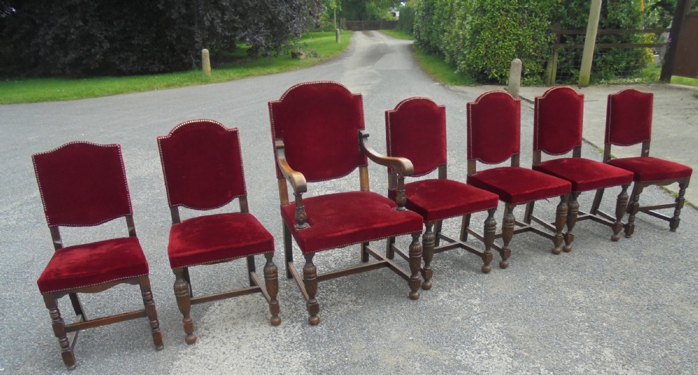 A set of seven late Victorian oak dining chairs upholstered in deep crimson velvet with brass studding, comprising six side chairs and one carver armchair.