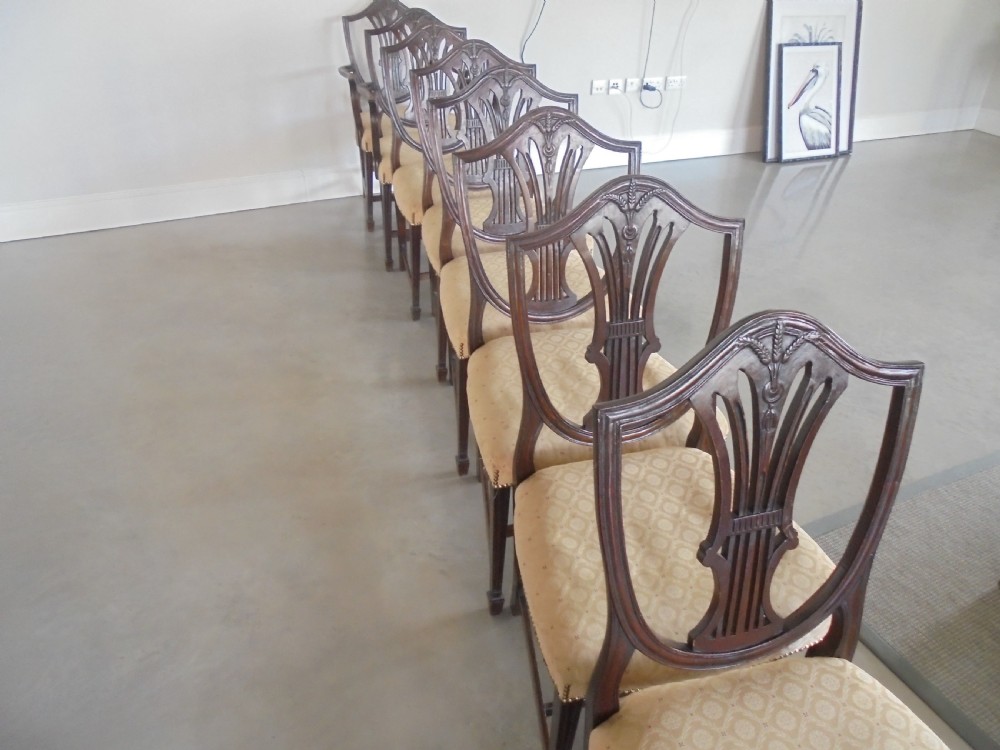 A set of eight dark mahogany dining chairs featuring carved shield backs, tapered square legs, and cream upholstered seats, including two armchairs and six side chairs. View II