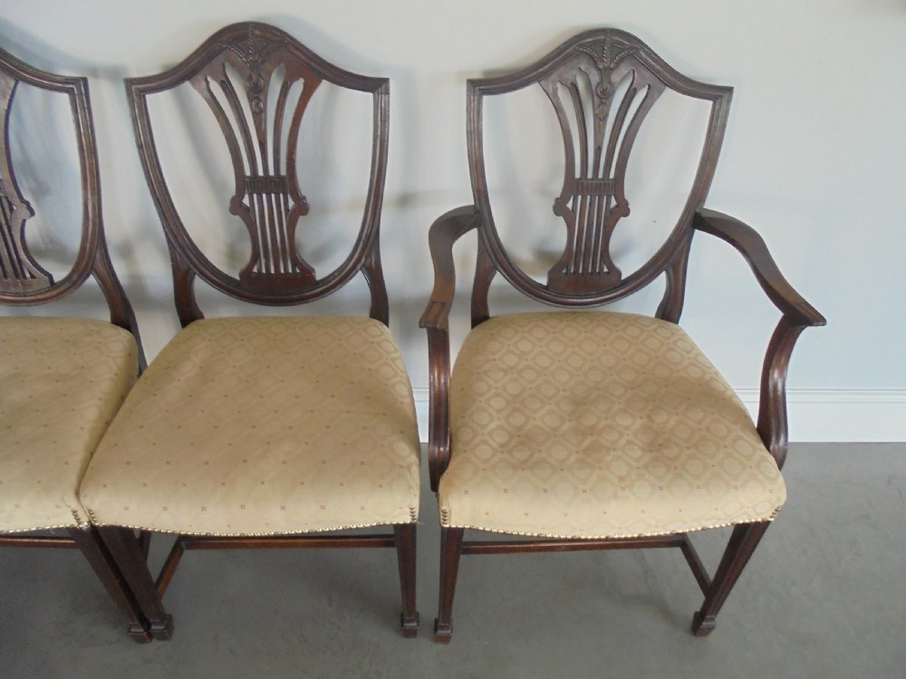 A set of eight dark mahogany dining chairs featuring carved shield backs, tapered square legs, and cream upholstered seats, including two armchairs and six side chairs. View III