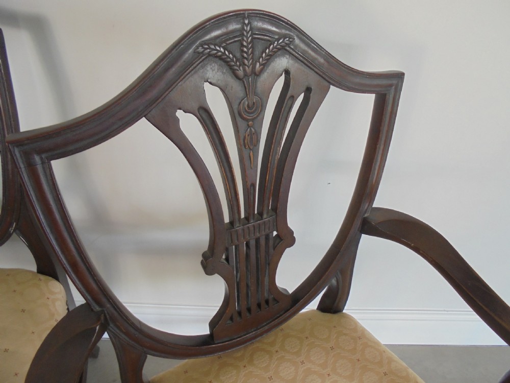 A set of eight dark mahogany dining chairs featuring carved shield backs, tapered square legs, and cream upholstered seats, including two armchairs and six side chairs. View VI