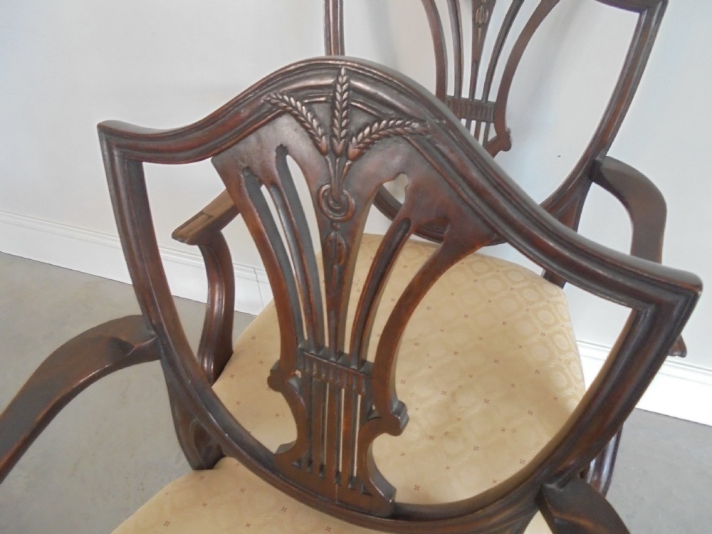 A set of eight dark mahogany dining chairs featuring carved shield backs, tapered square legs, and cream upholstered seats, including two armchairs and six side chairs. View X