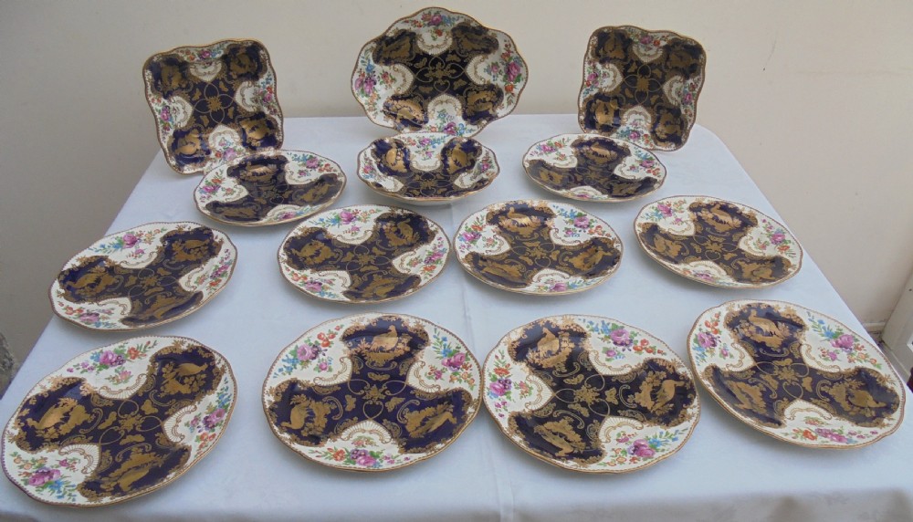 A fourteen-piece 19th-century porcelain part dessert service decorated with cobalt blue reserves, heavy gilt scrollwork, scalloped edges, and floral panels.