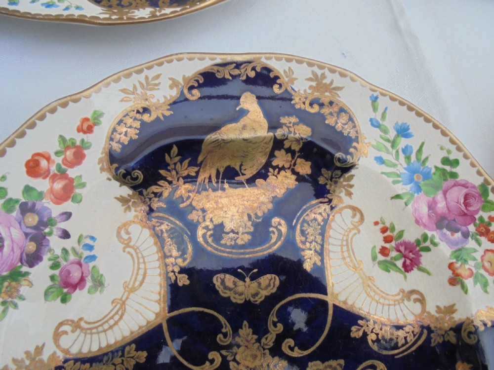 A fourteen-piece 19th-century porcelain part dessert service decorated with cobalt blue reserves, heavy gilt scrollwork, scalloped edges, and floral panels. View V