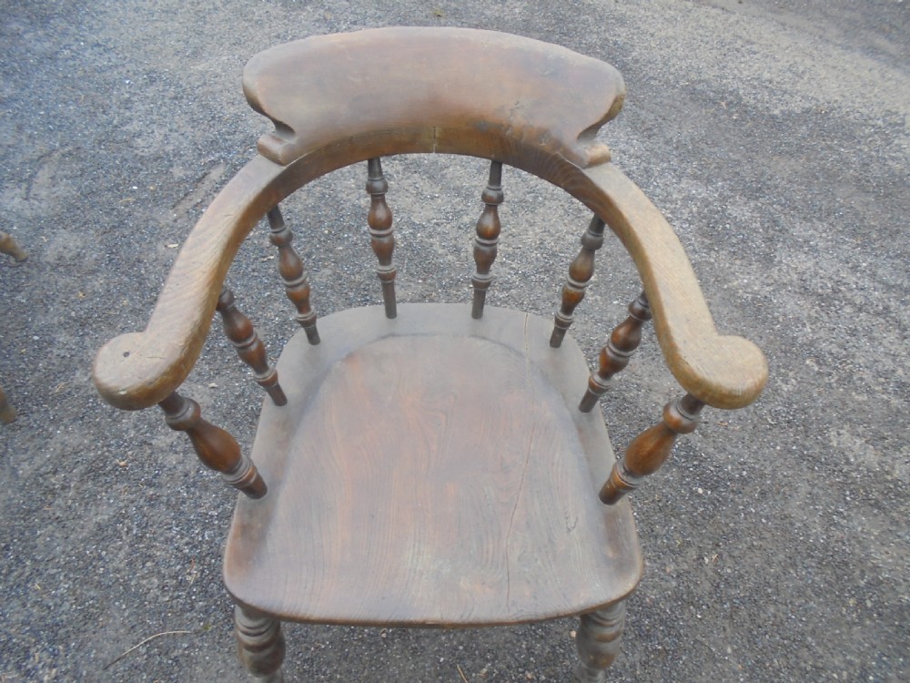 An antique ash and elm smokers bow armchair featuring a curved horseshoe armrest, turned spindles, a contoured solid saddle seat, and turned legs.