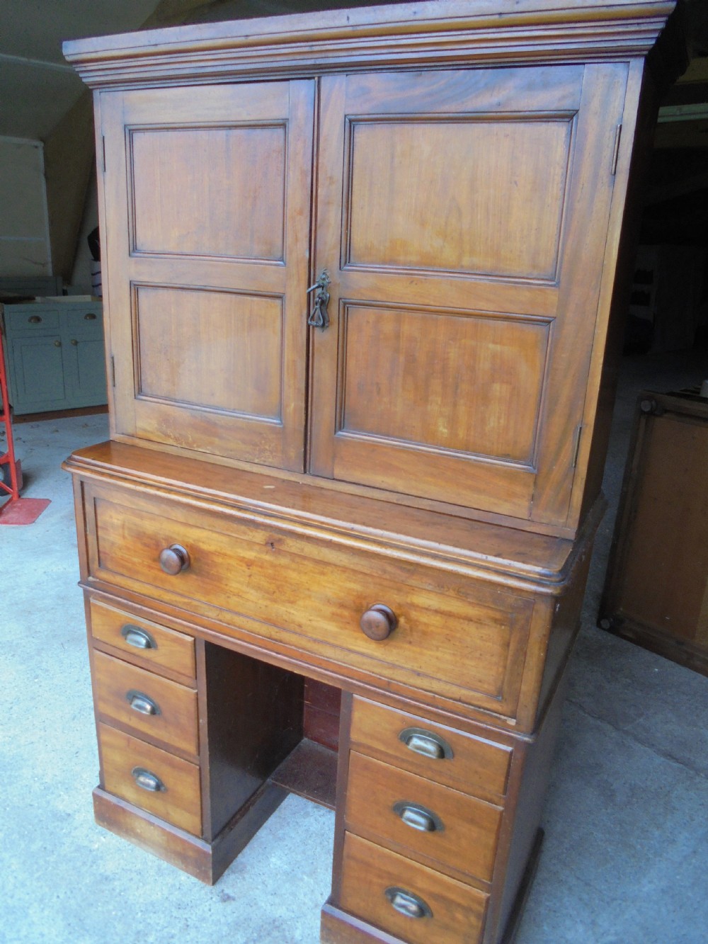 A Victorian mahogany post masters desk featuring a two-door upper cabinet above a central wide drawer and twin pedestal drawers with metal cup handles.