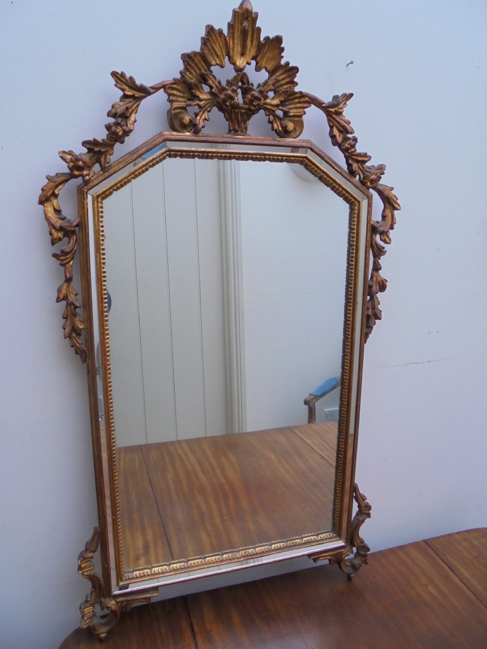 A large vertical wall mirror featuring an ornate carved giltwood frame with openwork acanthus scrolls, decorative floral cresting, and a bevelled mirror plate.