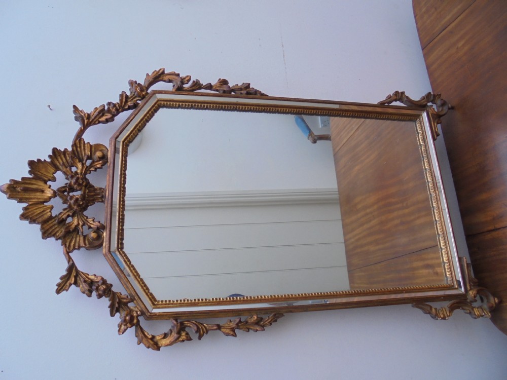 A large vertical wall mirror featuring an ornate carved giltwood frame with openwork acanthus scrolls, decorative floral cresting, and a bevelled mirror plate. View II