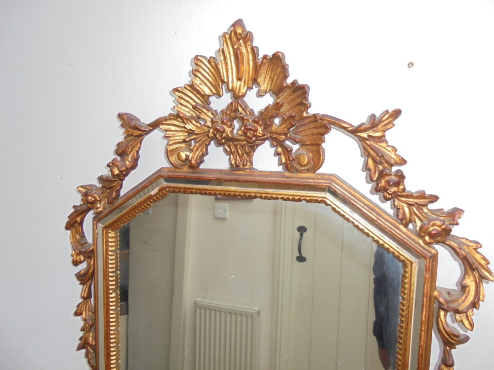 A large vertical wall mirror featuring an ornate carved giltwood frame with openwork acanthus scrolls, decorative floral cresting, and a bevelled mirror plate. View III