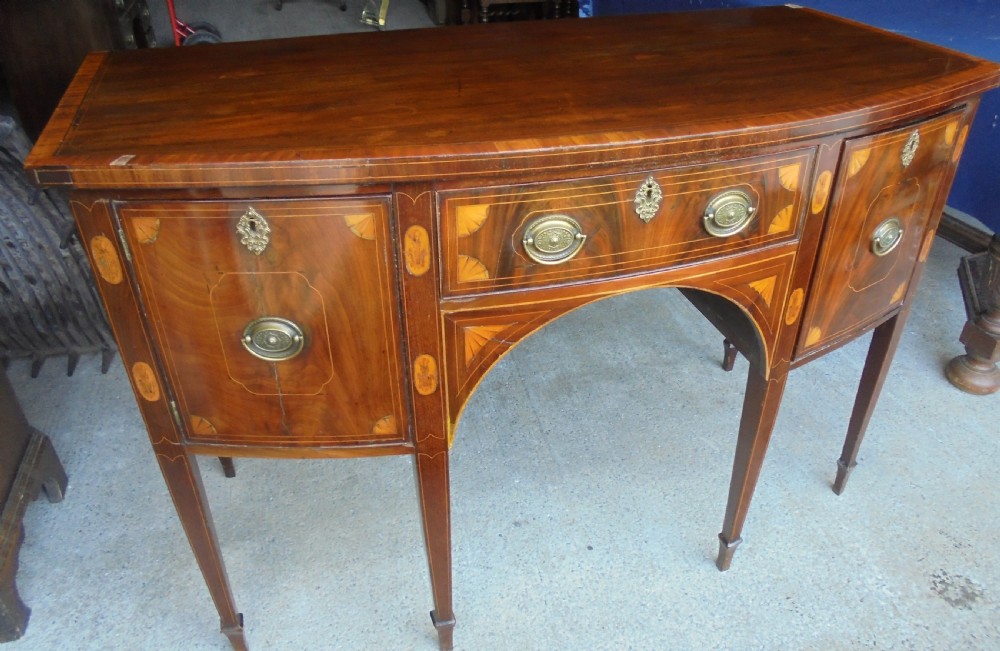 An 18th-century Sheraton style bowfront mahogany sideboard featuring satinwood inlays, brass drop handles, and square tapered legs. View II