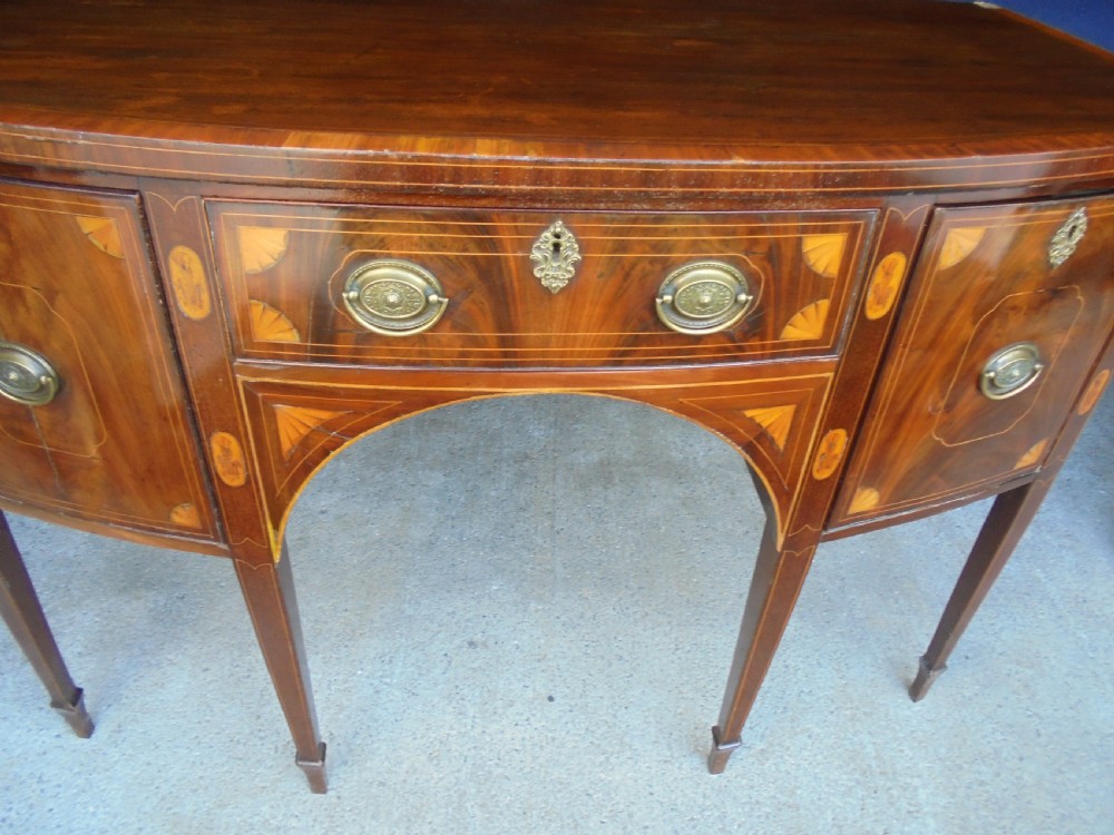 An 18th-century Sheraton style bowfront mahogany sideboard featuring satinwood inlays, brass drop handles, and square tapered legs. View III