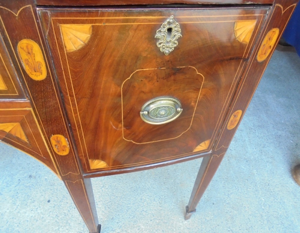 An 18th-century Sheraton style bowfront mahogany sideboard featuring satinwood inlays, brass drop handles, and square tapered legs. View IV