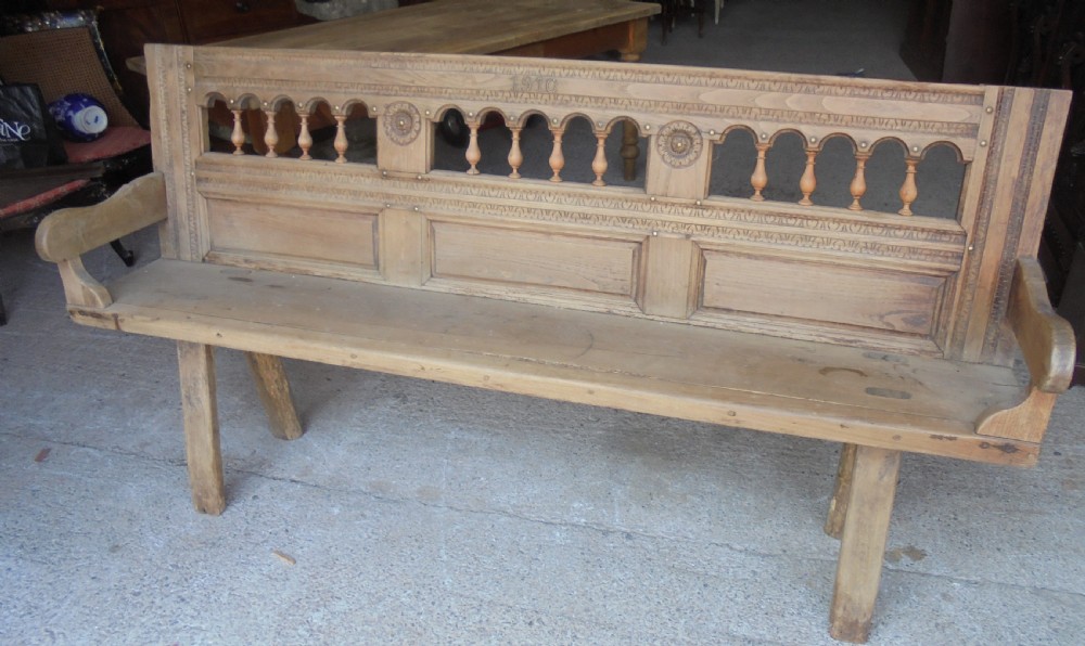 A natural light timber French country bench featuring a carved backrest with small turned spindles and panelled sections.