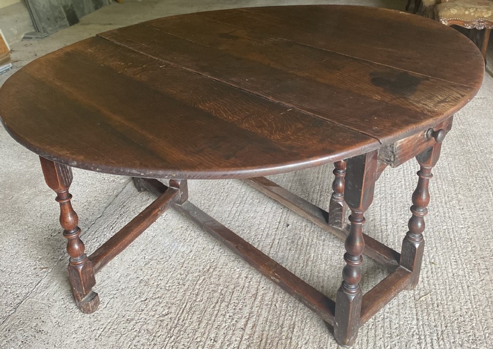 A seventeenth-century oak gateleg dining table featuring two oval drop leaves, turned legs, an end drawer, and square stretchers.