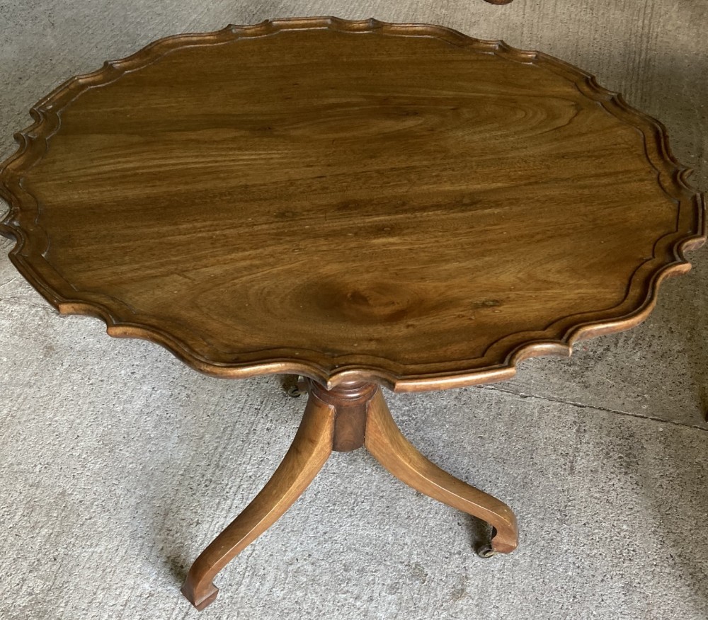 A 19th-century mahogany tripod table featuring a circular pie crust scalloped rim supported by a turned central pedestal and three splayed legs on castors.