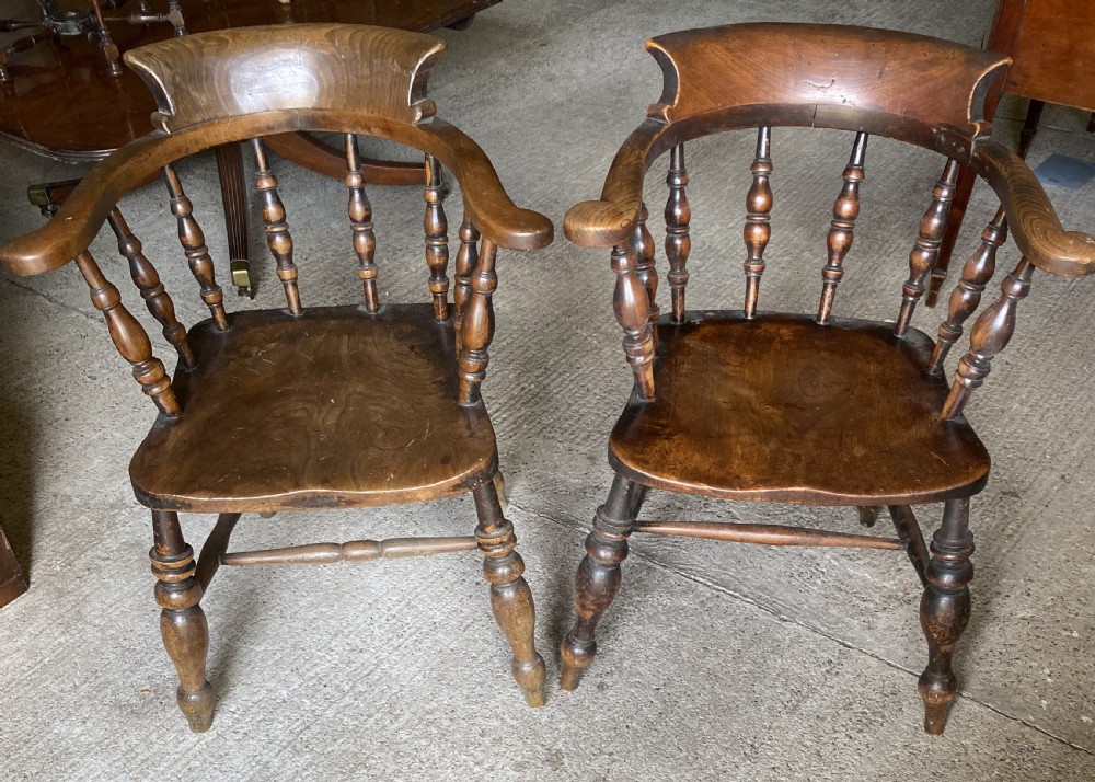 A near pair of 19th-century ash and elm smokers Captain chairs with curved crest rails, turned spindles, saddle seats, and turned legs.