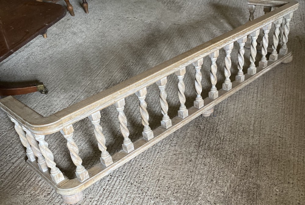 A wide limed oak fire fender featuring a row of twisted barley spindle balusters set between a top rail and bottom frame. View II