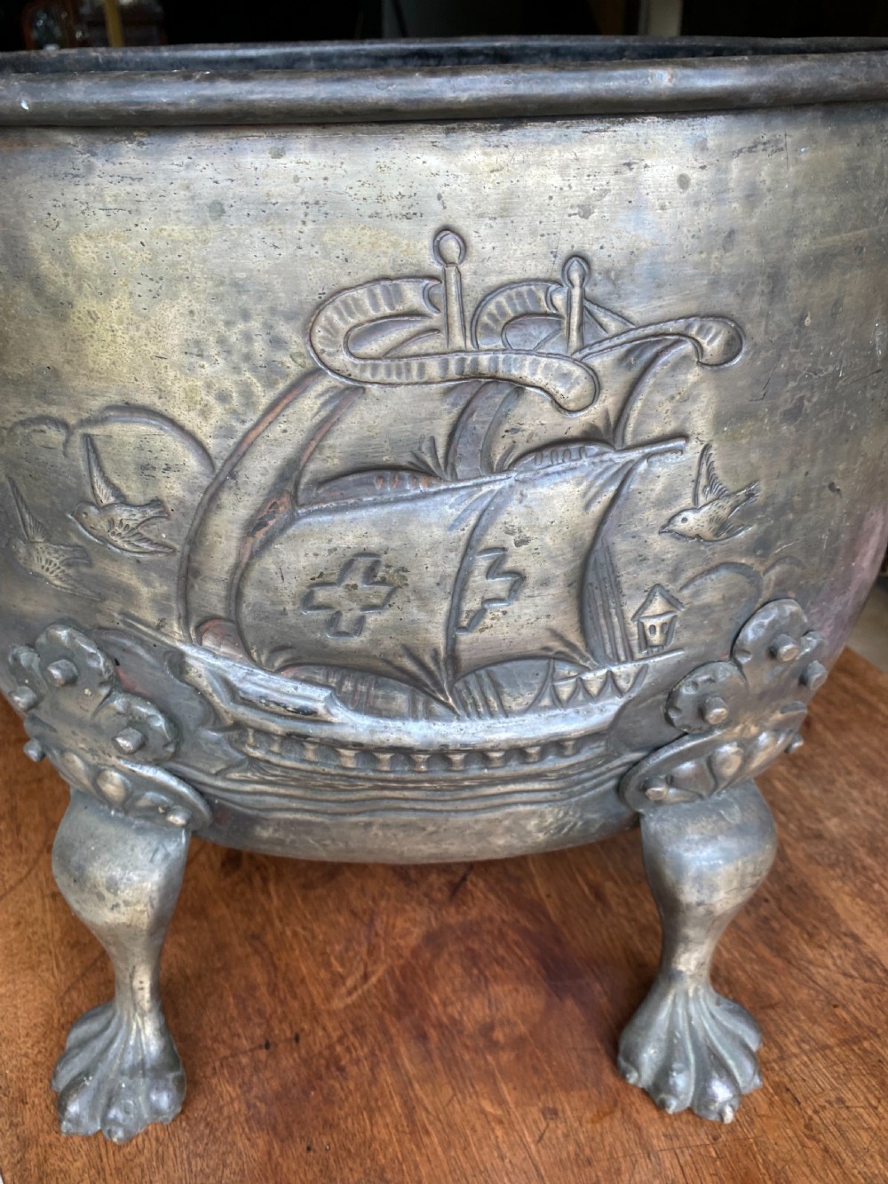A deep bronzed brass log bucket decorated with a relief depiction of a sailing ship, supported by claw feet and featuring lion mask side handles. View VI