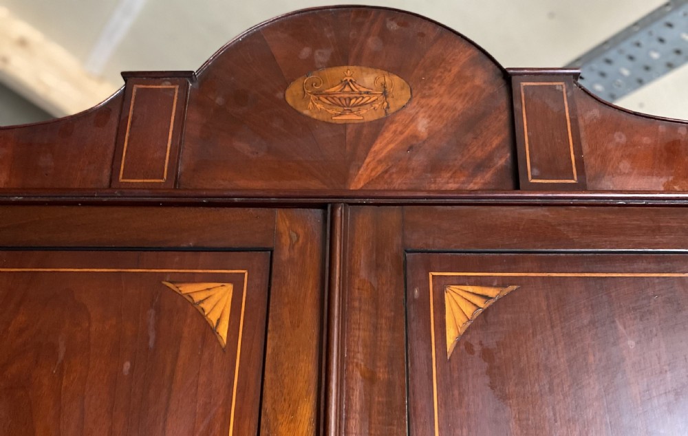 A tall Sheraton style mahogany double wardrobe with twin panelled doors adorned with satinwood urn inlays and a shaped pediment. View III