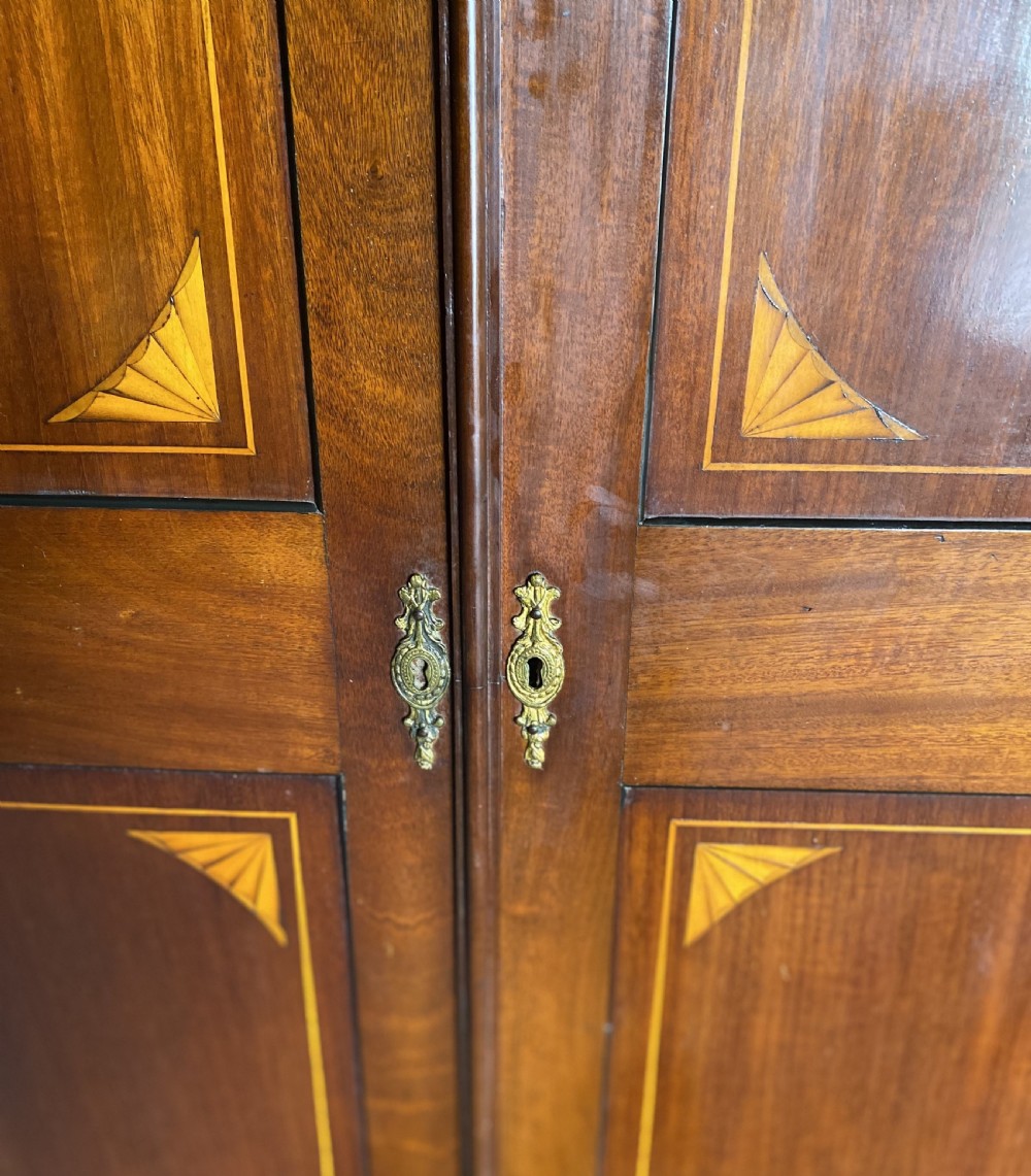 A tall Sheraton style mahogany double wardrobe with twin panelled doors adorned with satinwood urn inlays and a shaped pediment. View V