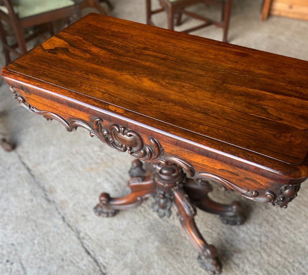 A Victorian rosewood fold-over card table featuring an intricately carved apron, turned central pedestal column, and four scrolled carved legs. View II