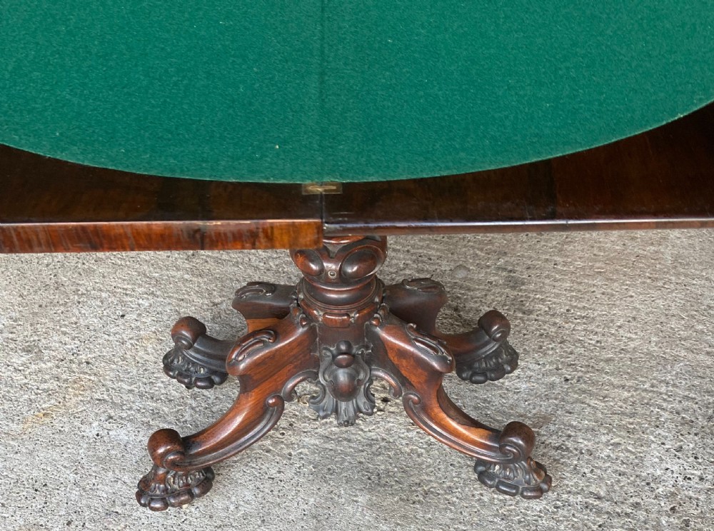 A Victorian rosewood fold-over card table featuring an intricately carved apron, turned central pedestal column, and four scrolled carved legs. View III