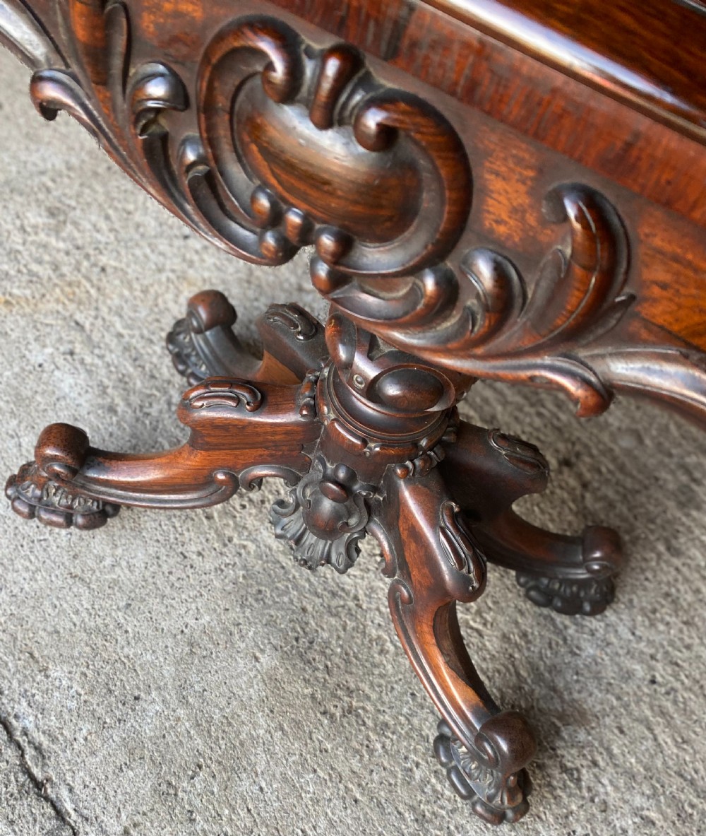 A Victorian rosewood fold-over card table featuring an intricately carved apron, turned central pedestal column, and four scrolled carved legs. View V