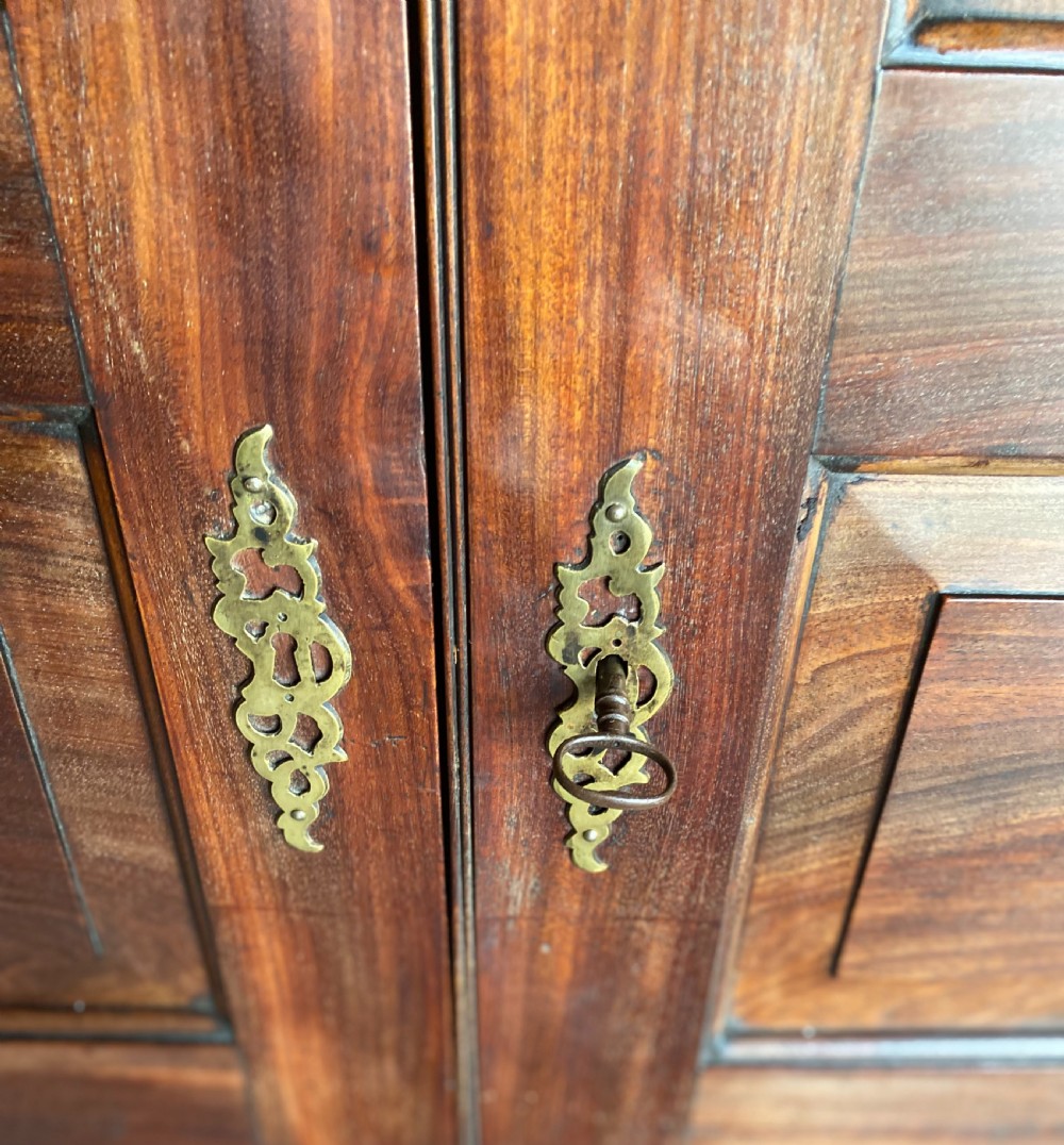 An 18th-century flame mahogany Channel Island press cupboard with double fielded panel doors, brass escutcheons, and a shaped lower apron. View II