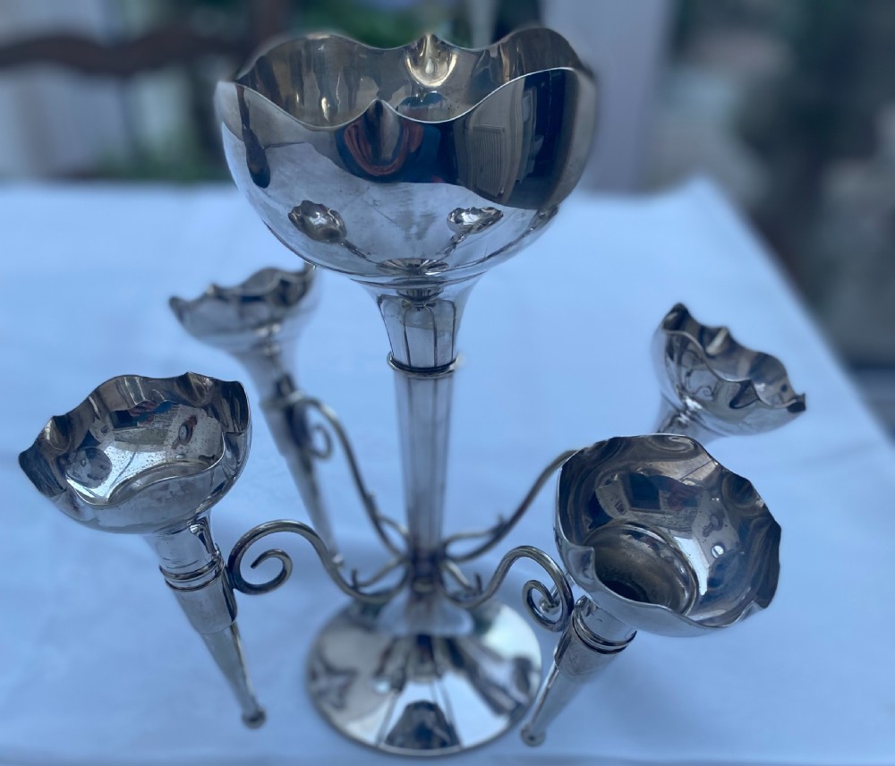 A silver-plated five-trumpet table epergne featuring a central tall trumpet vase surrounded by four smaller branching fluted vases on scroll arms.