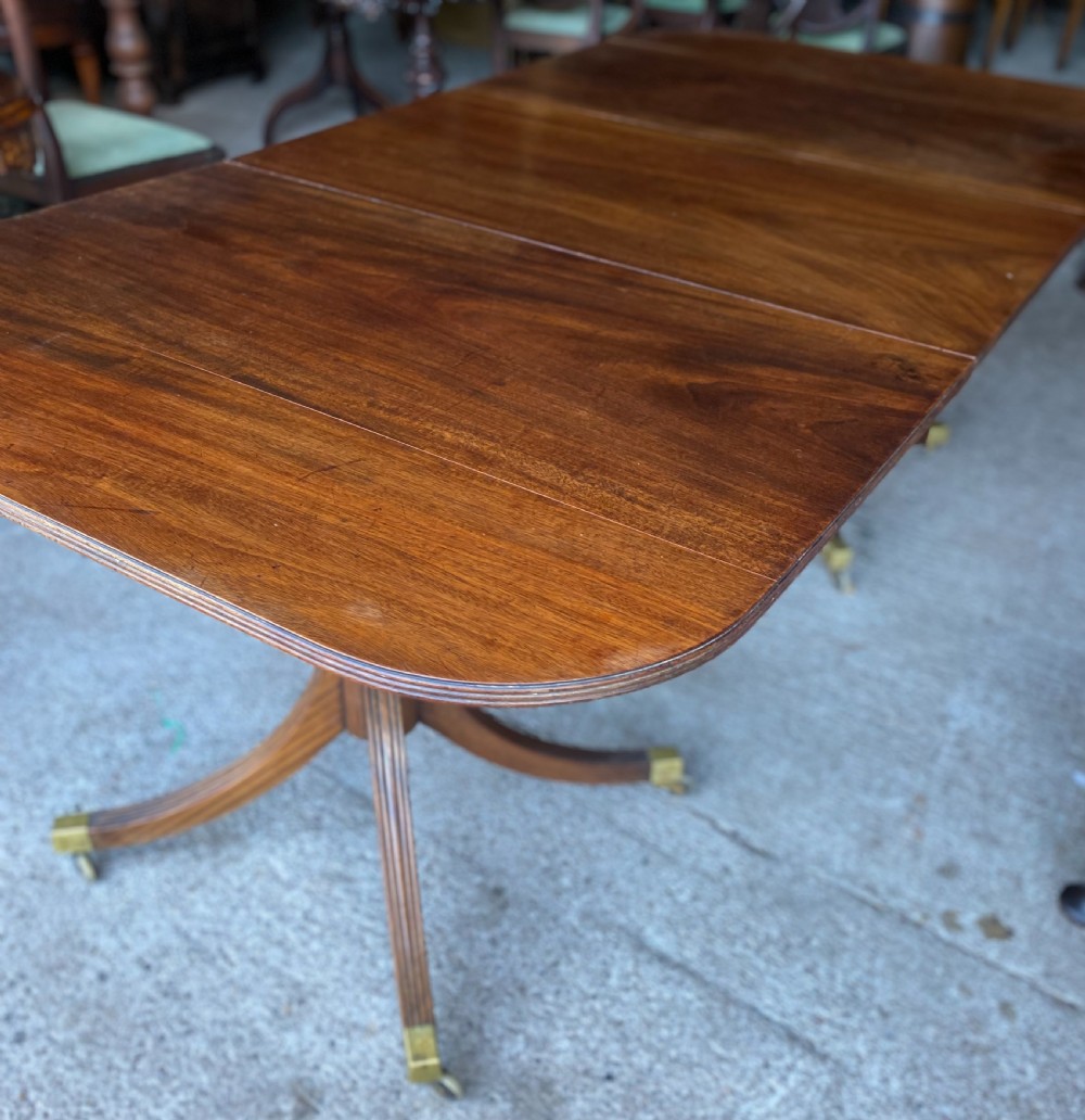 A 19th-century mahogany twin pillar dining table featuring reeded splayed legs, brass toe caps, and rounded tabletop corners.