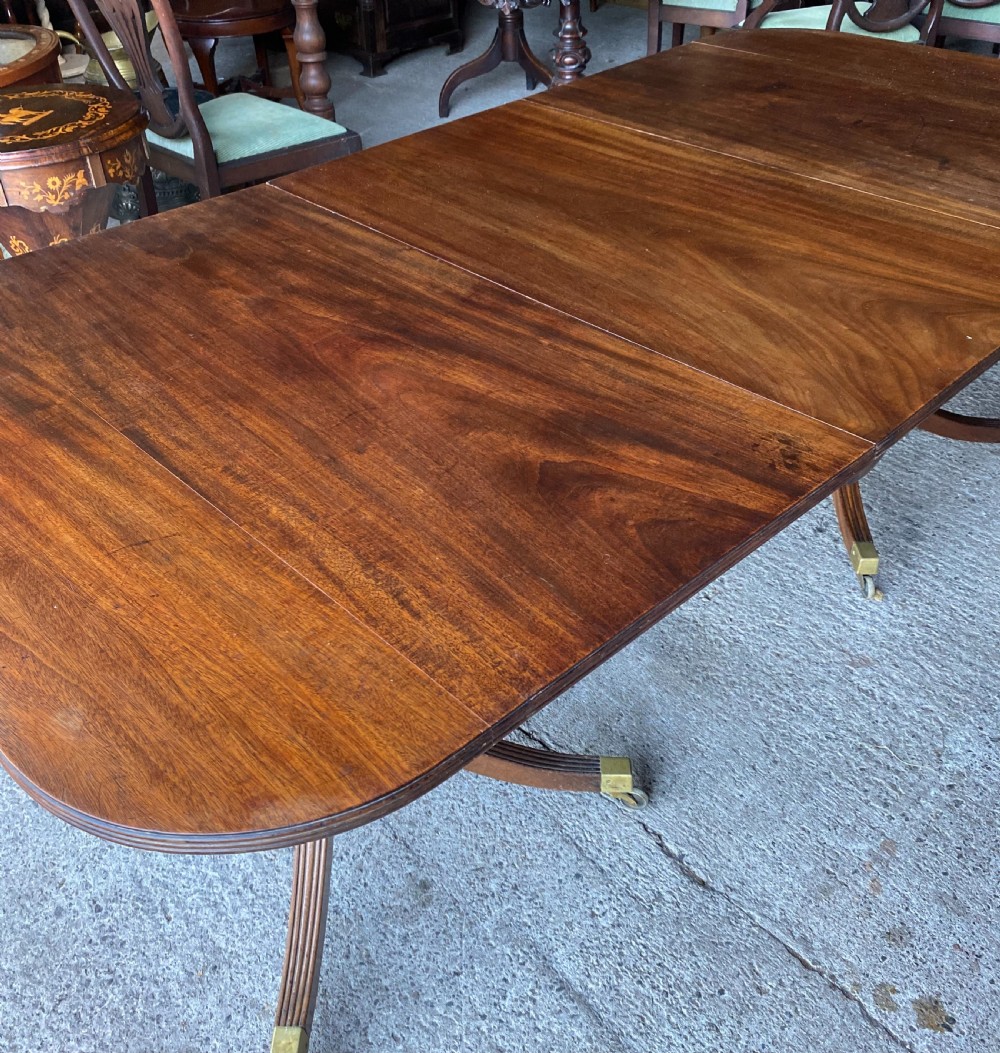 A 19th-century mahogany twin pillar dining table featuring reeded splayed legs, brass toe caps, and rounded tabletop corners. View V