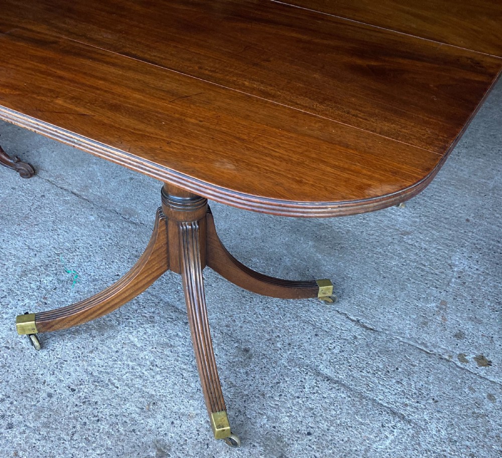 A 19th-century mahogany twin pillar dining table featuring reeded splayed legs, brass toe caps, and rounded tabletop corners. View VI