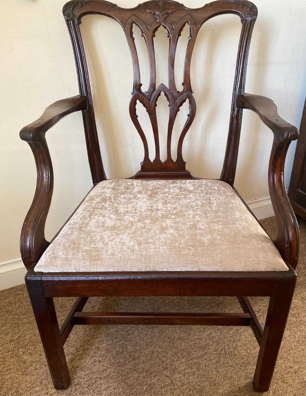 An 18th-century Chippendale mahogany armchair with a pierced carved back splat, swept arms, and a beige upholstered drop-in seat pad.