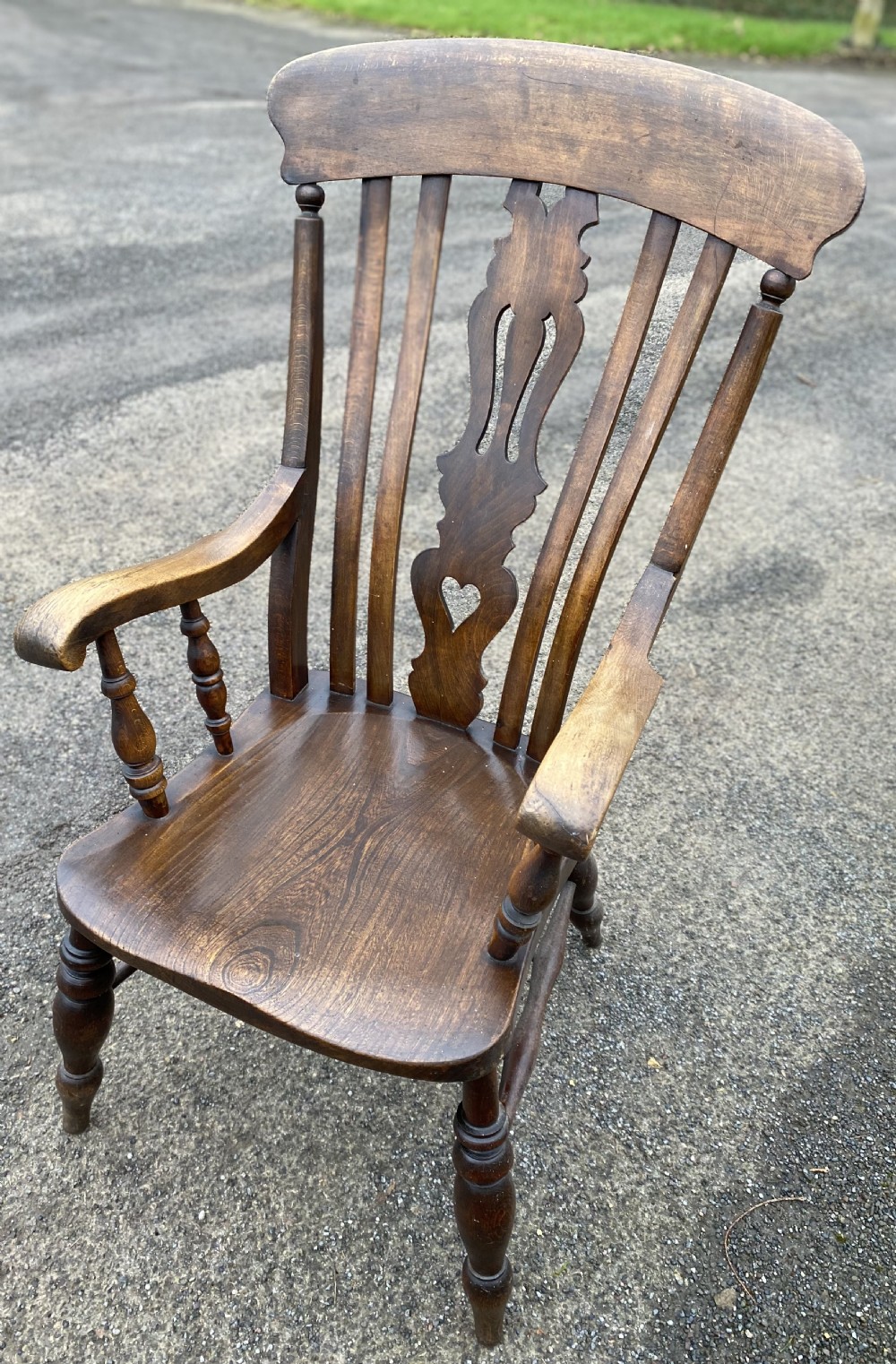 An antique wooden armchair with shaped armrests, turned legs, a contoured saddle seat, and a central back splat with a pierced heart detail. View II