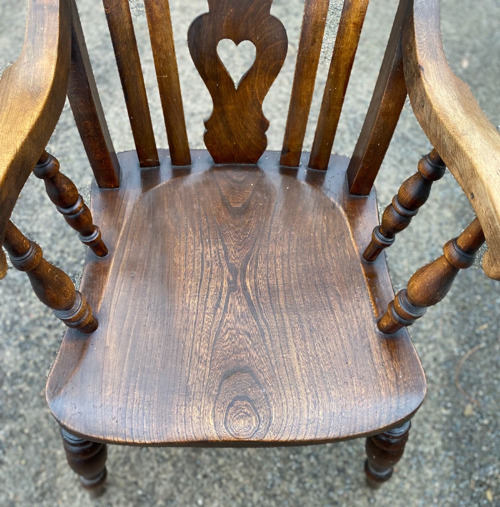 An antique wooden armchair with shaped armrests, turned legs, a contoured saddle seat, and a central back splat with a pierced heart detail. View IV
