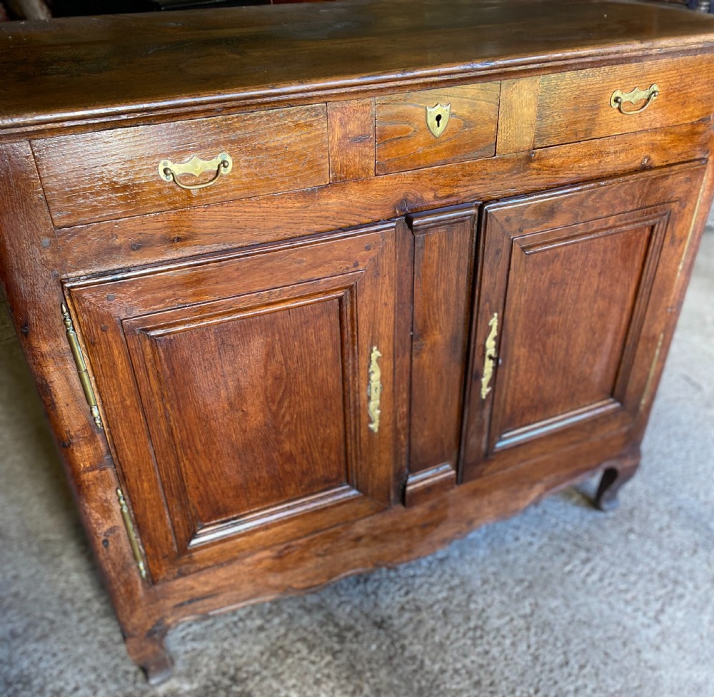 An early 18th-century French cedarwood dresser base featuring two panelled cupboard doors, long exterior brass hinges, upper drawers, and a warm brown patinated timber finish. View III