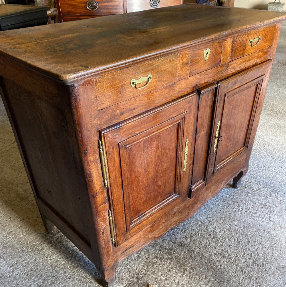 An early 18th-century French cedarwood dresser base featuring two panelled cupboard doors, long exterior brass hinges, upper drawers, and a warm brown patinated timber finish.