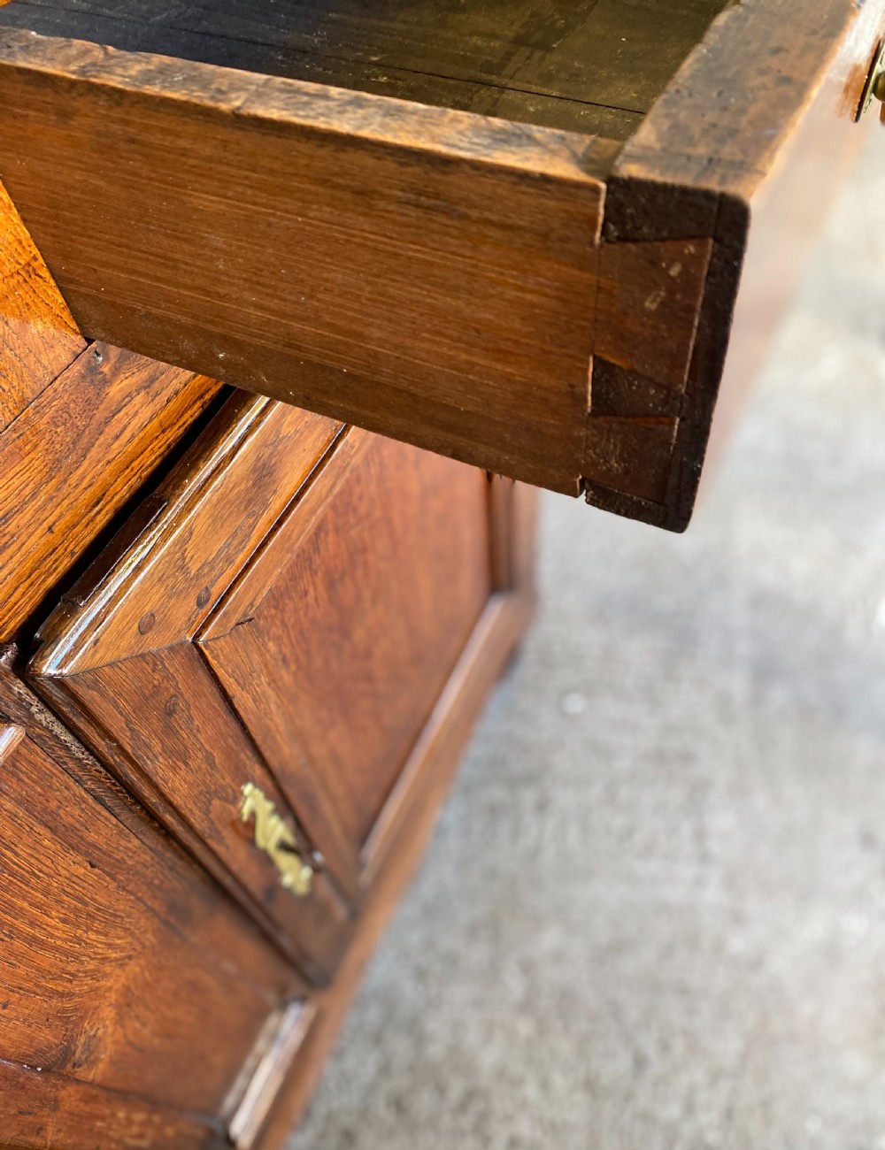 An early 18th-century French cedarwood dresser base featuring two panelled cupboard doors, long exterior brass hinges, upper drawers, and a warm brown patinated timber finish. View V