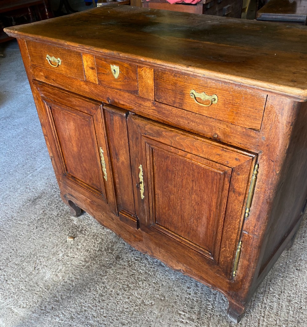 An early 18th-century French cedarwood dresser base featuring two panelled cupboard doors, long exterior brass hinges, upper drawers, and a warm brown patinated timber finish. View VI