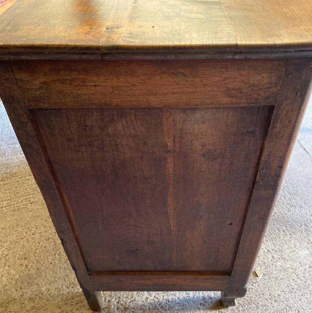 An early 18th-century French cedarwood dresser base featuring two panelled cupboard doors, long exterior brass hinges, upper drawers, and a warm brown patinated timber finish. View VIII