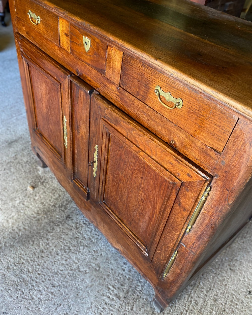 An early 18th-century French cedarwood dresser base featuring two panelled cupboard doors, long exterior brass hinges, upper drawers, and a warm brown patinated timber finish. View IX