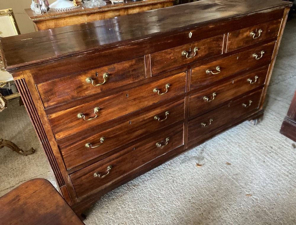 An eighteenth-century mahogany storage chest featuring a hinged top lid, multiple faux drawer fronts, brass swan-neck handles, key escutcheons, and fluted corner pilasters. View V