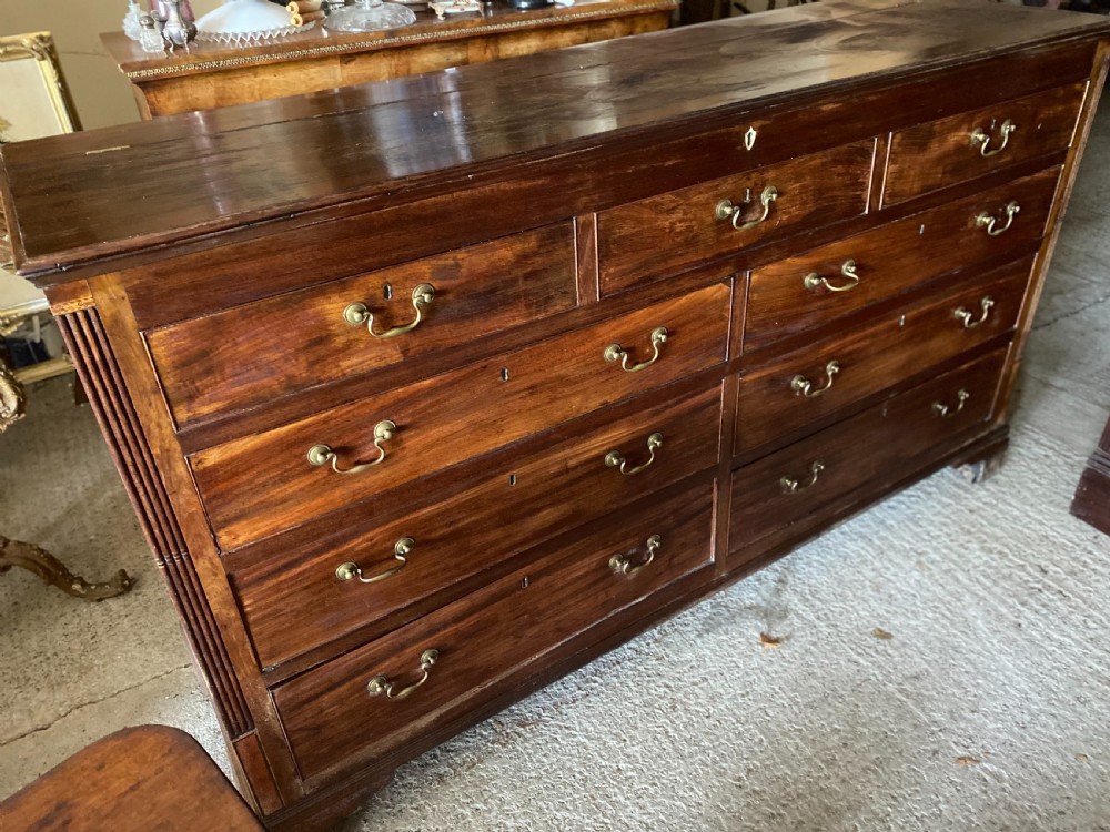 An eighteenth-century mahogany storage chest featuring a hinged top lid, multiple faux drawer fronts, brass swan-neck handles, key escutcheons, and fluted corner pilasters. View VI