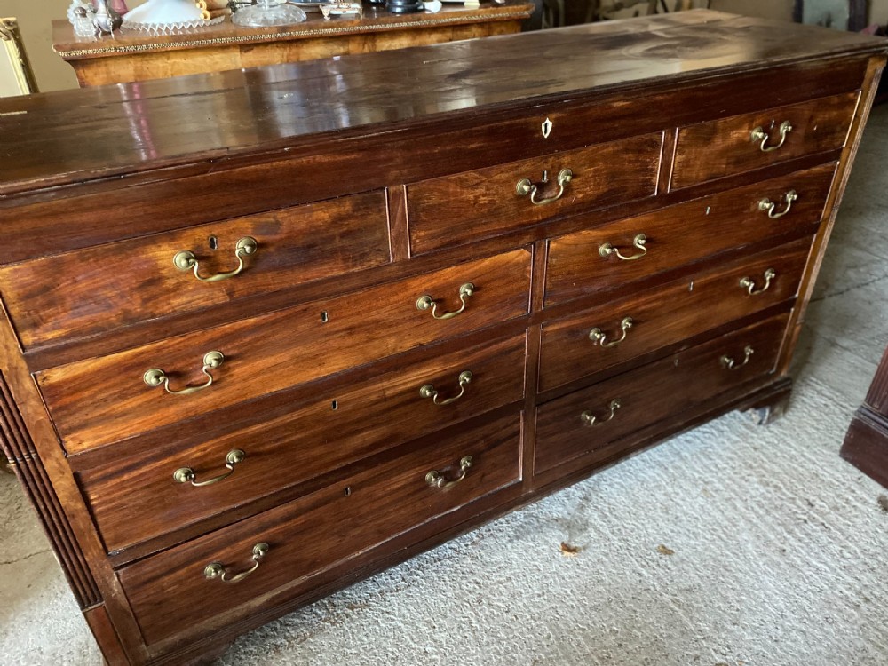 An eighteenth-century mahogany storage chest featuring a hinged top lid, multiple faux drawer fronts, brass swan-neck handles, key escutcheons, and fluted corner pilasters. View VII